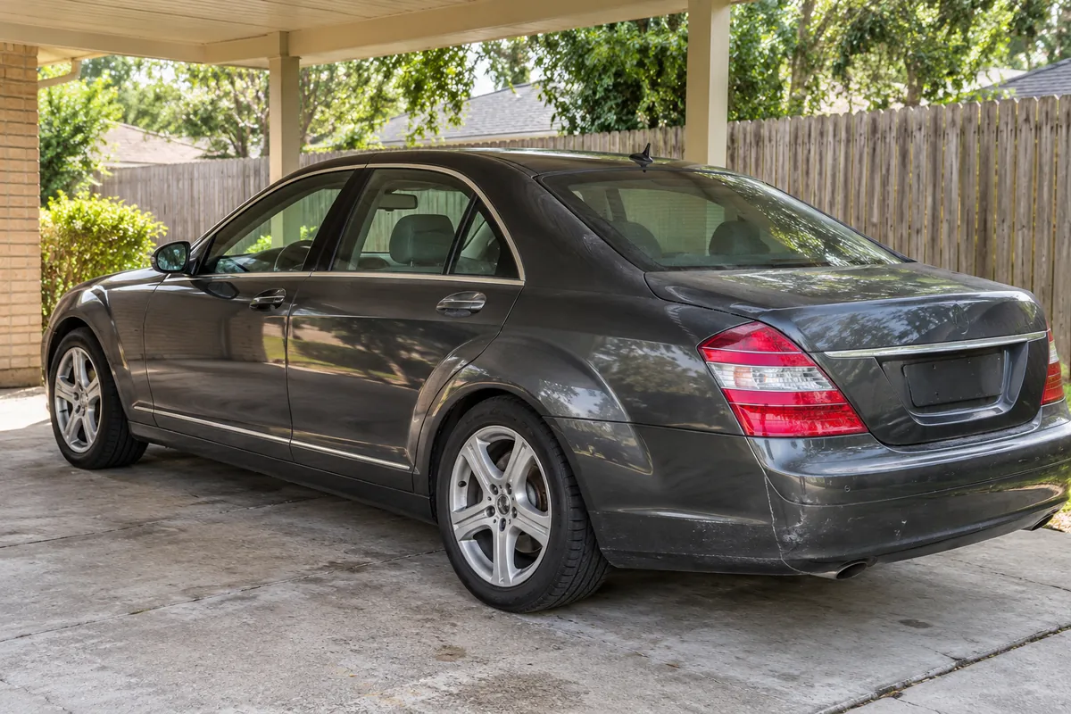 Illustrative dark gray aging luxury sedan in plain covered residential carport
